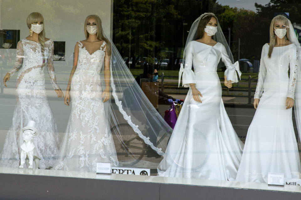 FILE - A masked cyclist is reflected in the window of a wedding dress store with mannequins wearing face masks, in Zagreb, Croatia on April 23, 2020. Now that weddings have slowly cranked up under a patchwork of ever-shifting restrictions, horror stories from vendors are rolling in. Many are desperate to work after the coronavirus put an abrupt end to their incomes and feel compelled to put on their masks, grab their cameras and hope for the best. (AP Photo/Darko Bandic, File)