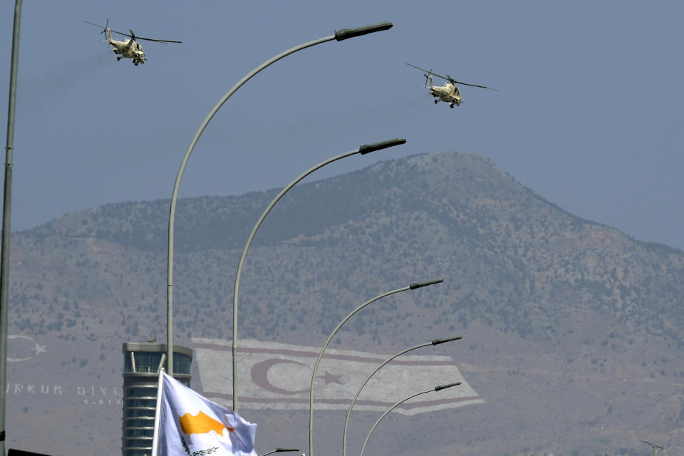 Military helicopters of Cypriot air forces fly over a military parade marking the 62nd anniversary of Cyprus' independence from British colonial rule, as the giant paintings of the Turkish and the Turkish Cypriot breakaway flags are seen on Pentadahtilos mountain in the Turkish occupied area in the background, in Nicosia, Cyprus, Saturday, Oct. 1, 2022. Cyprus gained independence from Britain in 1960 but was split along ethnic lines 14 years later when Turkey invaded following a coup aimed at uniting the island with Greece. (AP Photo/Petros Karadjias)