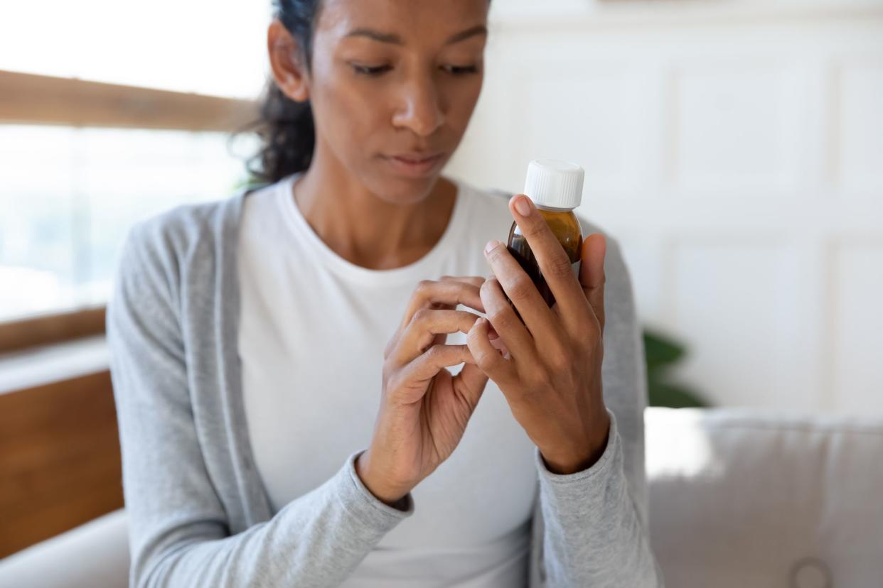 Young African American woman hold medication bottle reading instruction or prescription on packaging, millennial biracial female prepared to take medicine syrup, healthcare, pharmacy concept