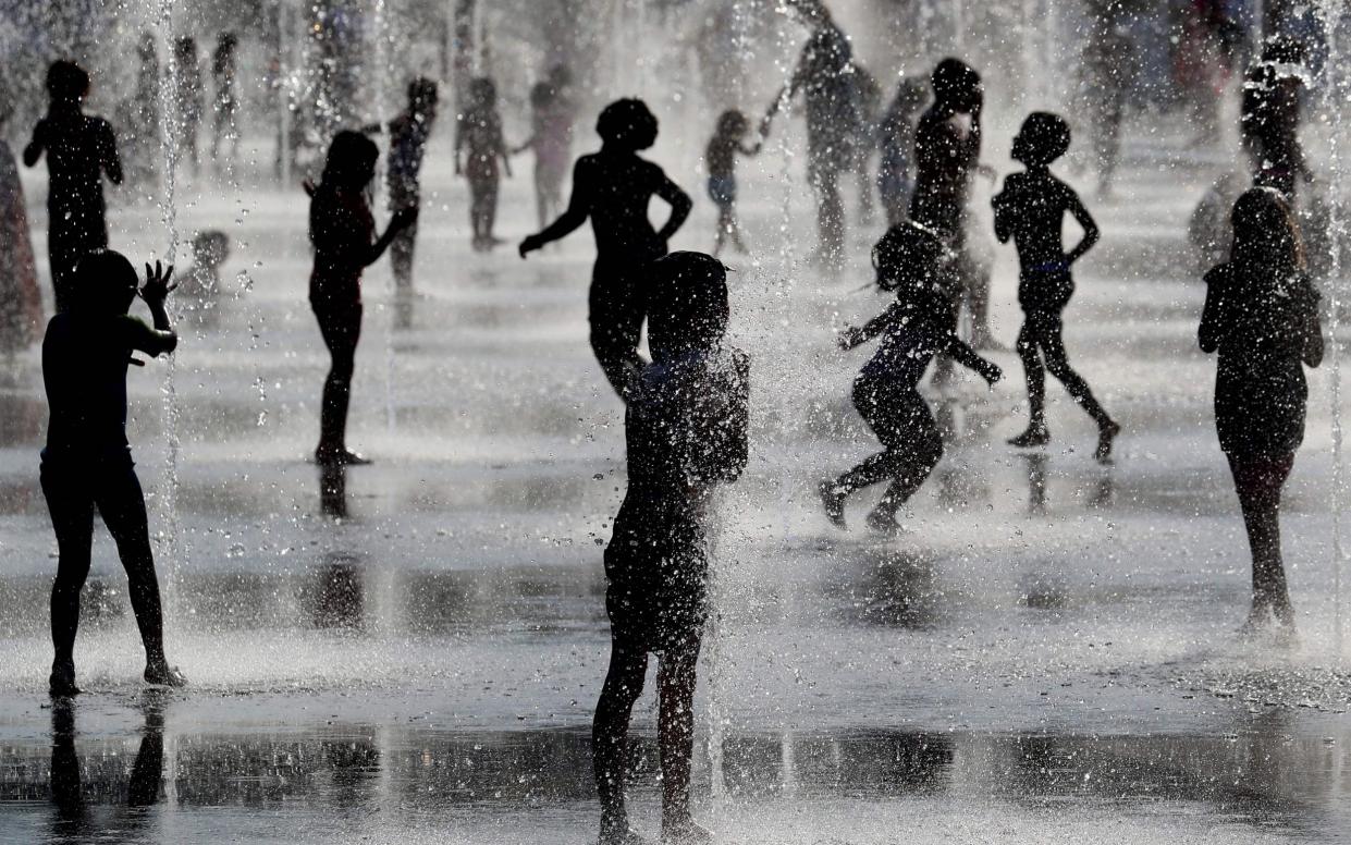 Children play under water jets in a fountain as they cool off during a heatwave in Nice