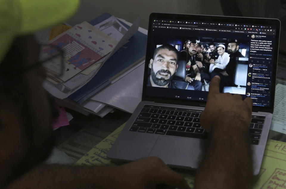 A member of a social media rights group shows a selfie photo of elite police officers taken with Khalid Khan, in white, a smiling gunman who shot and killed Tahir Naseem, a Pakistani-American, in a courtroom in Peshawar while standing trial on a charge of blasphemy, that went viral on the internet after the incident, at his office in Islamabad, Pakistan, Thursday, Aug. 20, 2020. Social media trackers say the lockdown, which lasted till early August, sparked a 50% increase in internet use in this conservative Muslim nation of over 220 million people — along with an explosion of hate speech and incitement. (AP Photo/Anjum Naveed)