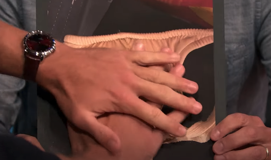 Close-up shot showing a person's hands holding up a photograph of underwear. No celebrity or red carpet present