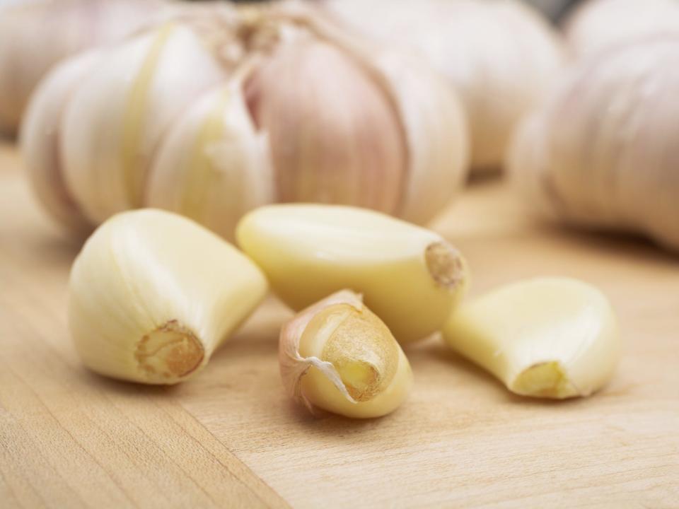 peeled garlic on a cutting board with whole garlic head in background