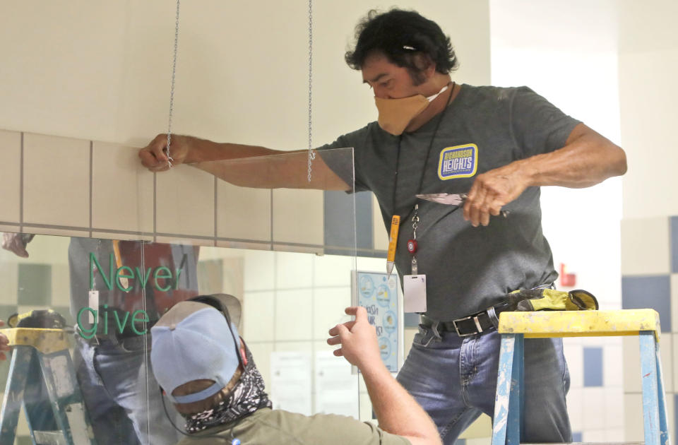 Richardson Independent School District workers Daniel Limon, right, and Matt Attaway install a plexiglass barrier in the restroom at Bukhair Elementary School in Dallas, Wednesday, July 15, 2020. Texas Education Commissioner Mike Morath told the state Board of Education on Tuesday that the annual State of Texas Assessments of Academic Readiness, also known as STAAR, will return in the 2020-2021 school year. (AP Photo/LM Otero)