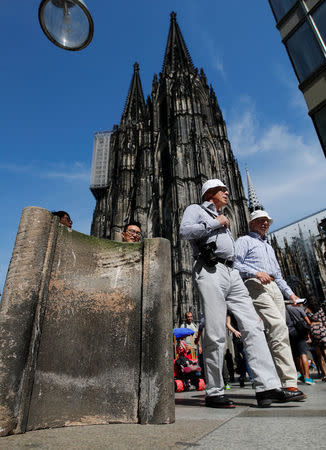 People walk past concrete barriers placed by police in front of the world famous gothic cathedral in Cologne, Germany, August 23, 2017. REUTERS/Wolfgang Rattay