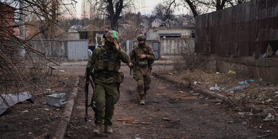 Two Ukrainian soldiers walk behind one another on a dirty street.