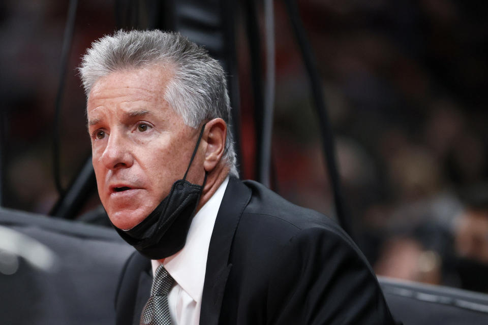 Neil Olshey, with a face mask down below his chin, looks on.