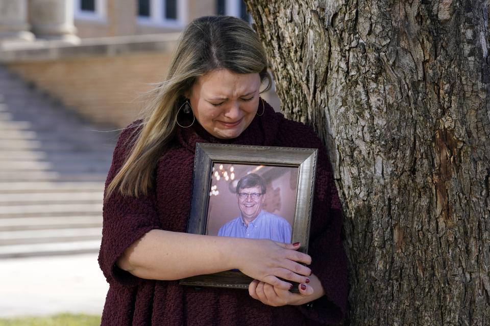 Katie Riggs Maxwell begins to cry as she hugs a portrait of her father Mark Riggs while posing for a photo, Wednesday, Dec. 16, 2020, on the campus of Abilene Christian University in Abilene, Texas. Mark Riggs, who was a professor at the school, passed away last Monday of COVID-19. (AP Photo/Tony Gutierrez)