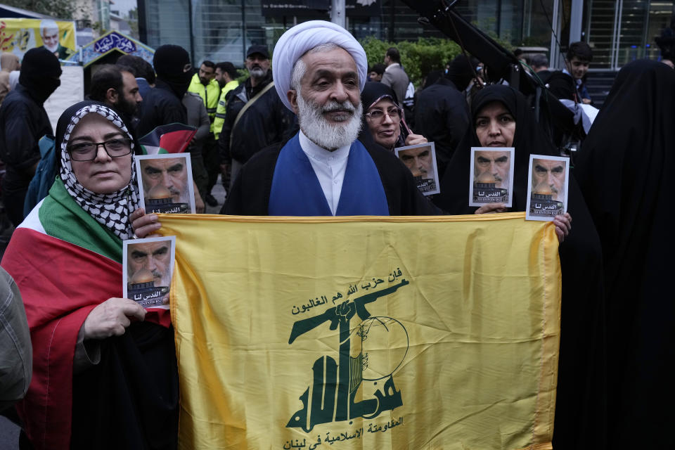 An Iranian cleric holds Lebanon's militant Hezbollah group flag and posters of the late Iranian revolutionary founder Ayatollah Khomeini and Jerusalem's Dome of the Rock during a rally in front of the former U.S. Embassy in Tehran, Iran, marking 44th anniversary of the seizure of the embassy by militant Iranian students, Saturday, Nov. 4, 2023. (AP Photo/Vahid Salemi)