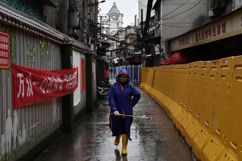 Community worker with sanitizing equipment disinfects the street next to barricades in Wuhan