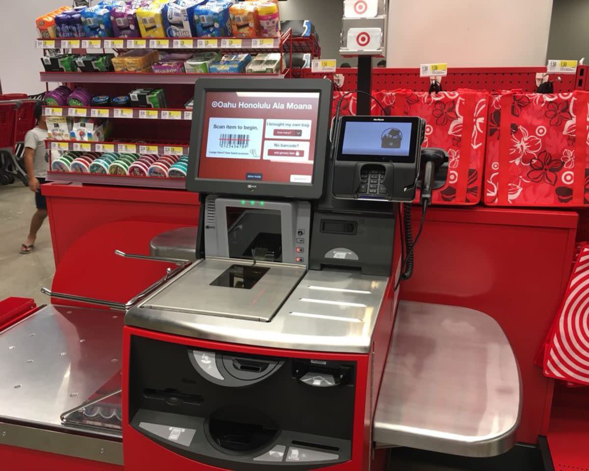 A self-service checkout in a Target store, top left many types of chewing gum for sale and top right red reusable bags