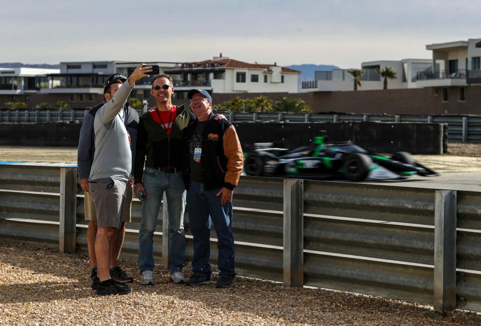 A group of men pose for a photo as Agustin Canapino of Juncos Hollinger Racing passes them coming through turn 17 during day two of NTT IndyCar Series open testing at The Thermal Club in Thermal, Calif., Friday, Feb. 3, 2023.