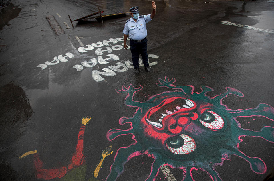 An Indian traffic policeman stands next to an artwork displayed on a road to create awareness about coronavirus during lockdown in Gauhati, India, Wednesday, April 15, 2020. (AP Photo/Anupam Nath)