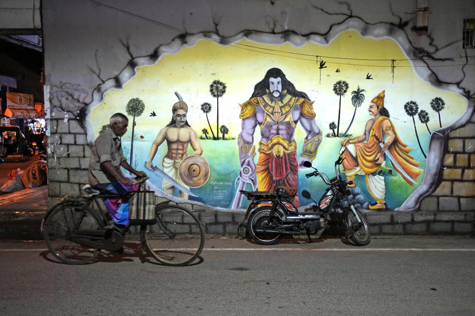 An ethnic Tamil rides his bicycle past a mural portraying a scene from an Hindu epic in Jaffna, Sri Lanka, May 4, 2024. (AP Photo/Eranga Jayawardena)