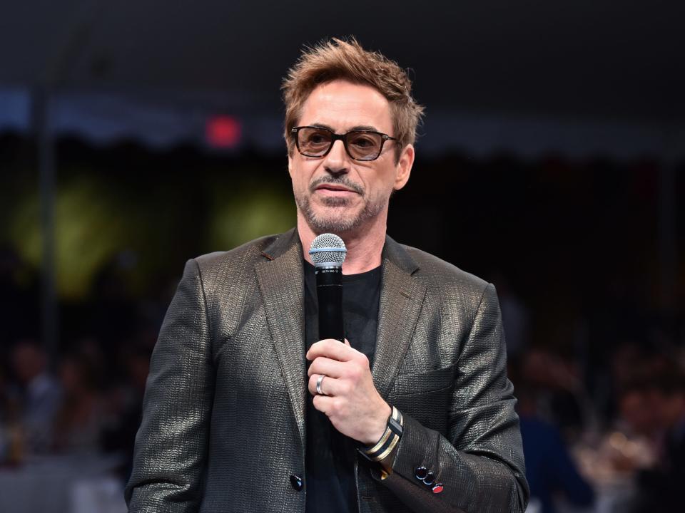 Robert Downey Jr. in grey suit, glasses, holding a micorphone