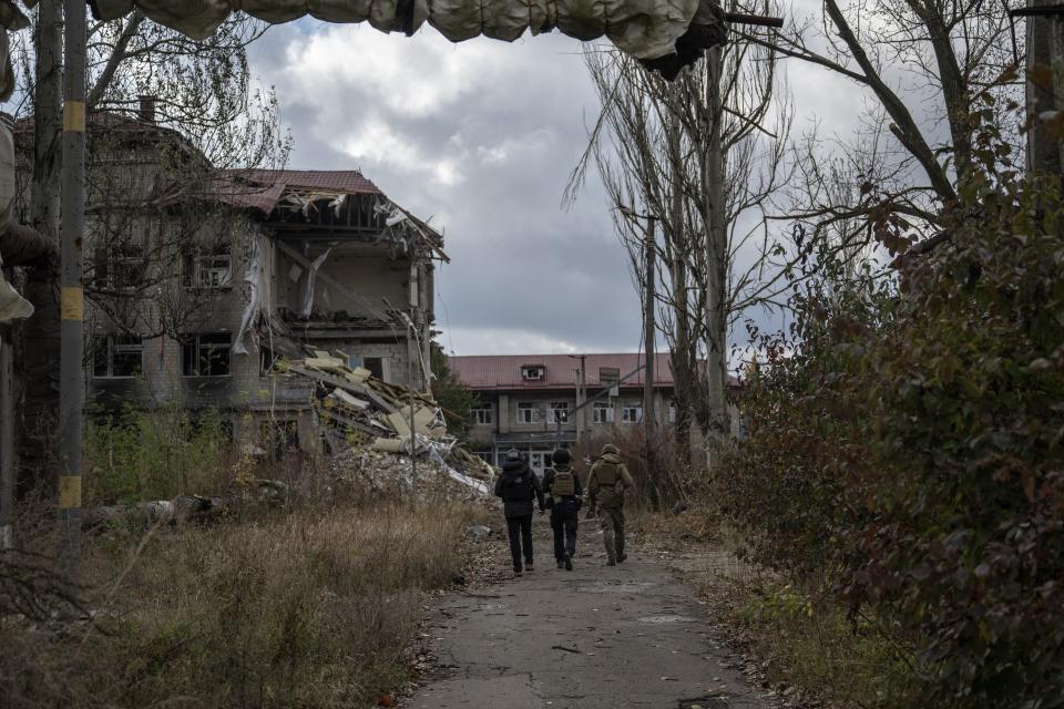 Three Ukrainians walk in the foreground of a destroyed building in Avidiivka, Donetsk (Anadolu via Getty Images)