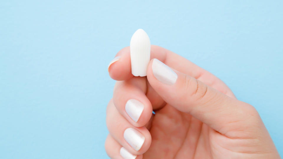 A close up of a woman with white nail polish holding a boric acid suppository, one of the best home remedies for bacterial vaginosis