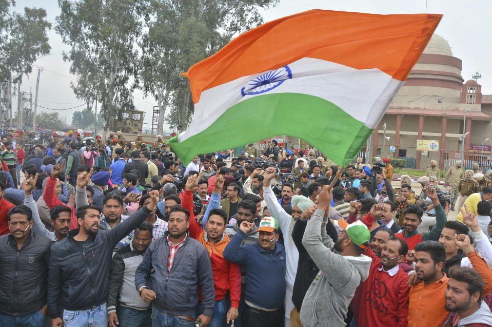 An Indian waves national flag as others shout slogans while they wait to welcome Indian pilot at India Pakistan border at Wagah, 28 kilometers (17.5 miles) from Amritsar, India, Friday, March 1, 2019. Pakistan is preparing to hand over a captured Indian pilot as shelling continued for a third night across the disputed Kashmir border even as the two nuclear-armed neighbors seek to defuse the most serious confrontation in two decades. (AP Photo/Prabhjot Gill)