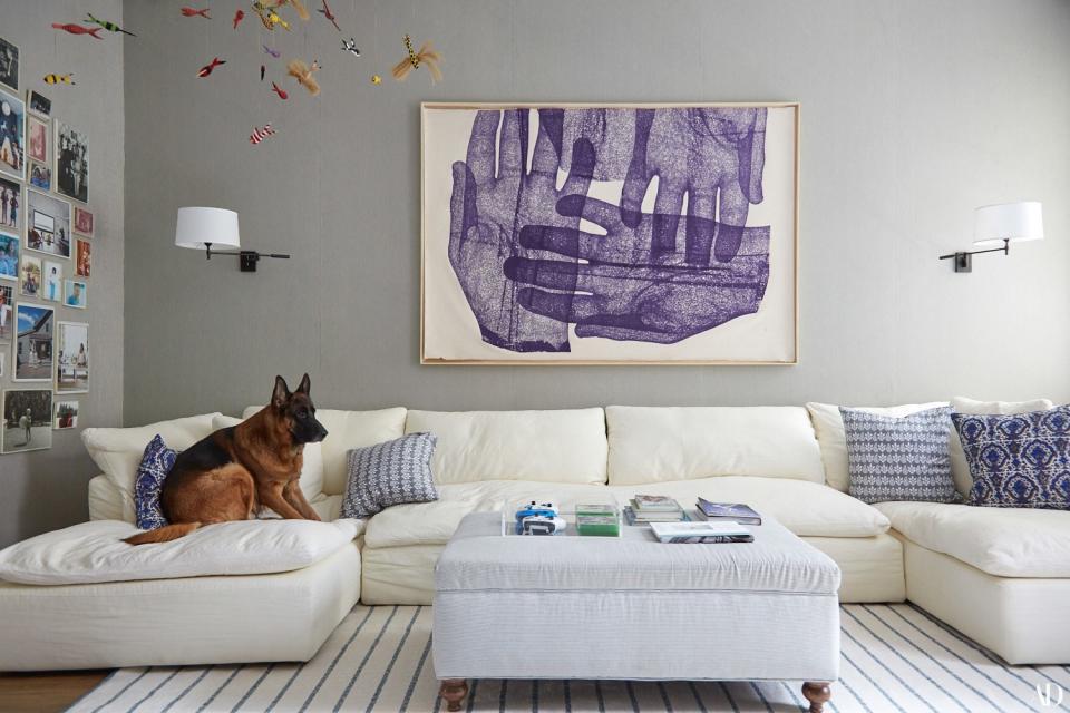 German shepherd Frank lounges on an RH sofa in the family room. The walls are swathed in vintage seersucker, which also covers the custom ottoman. Sconces from Circa Lighting; Richard Dupont artwork; rug by Crosby Street Studios.