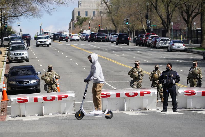 Una persona pasa sobre un scooter mientras los miembros de la Guardia Nacional y los agentes del orden vigilan las calles que rodean el Capitolio de Estados Unidos y los edificios de oficinas del Congreso luego de una amenaza a la seguridad en el Capitolio en Washington