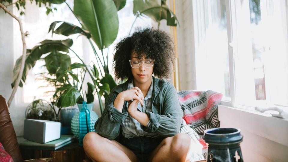 A woman relaxes in her house, eyes closed in prayer, deep thought, or meditation.