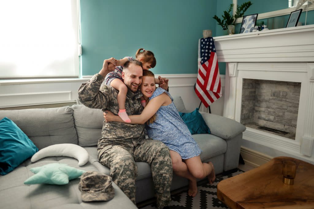 A military active member hugs his wife and kids while sitting on their couch at home.