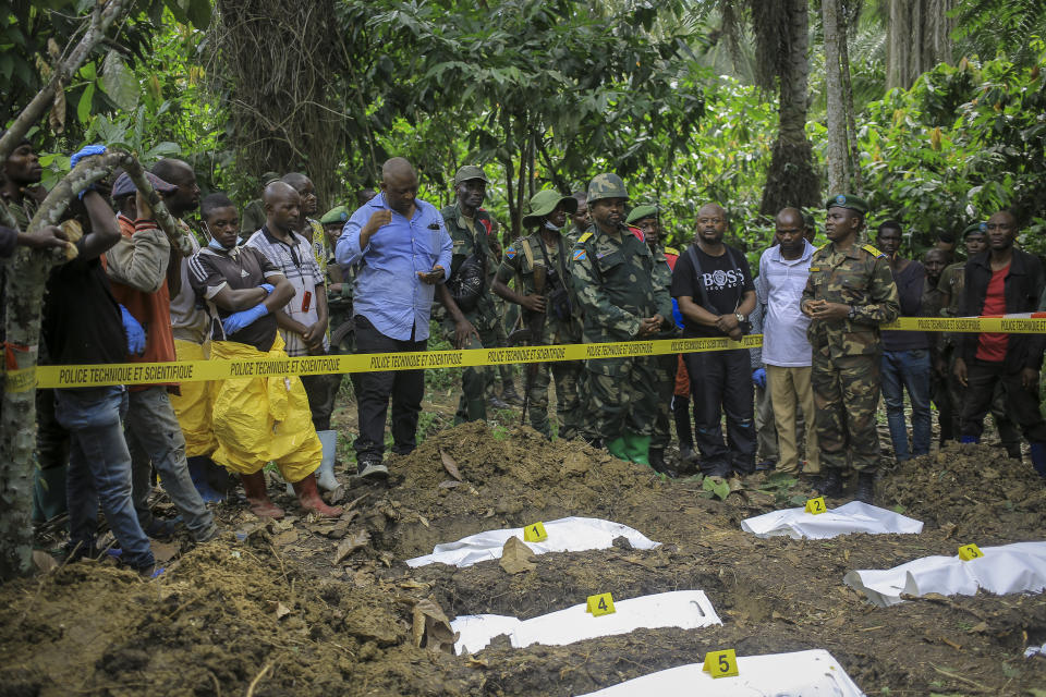 Military, forensics workers, and others observe human remains at a mass grave in the village of Ndoma, near Beni in North Kivu, Congo Saturday, May 6, 2023. The remains of at least 20 people were found buried in a mass grave in an area used to cultivate cacao in Ndoma village in Congo's North Kivu province this weekend, according to local authorities and a military spokesperson. (AP Photo)