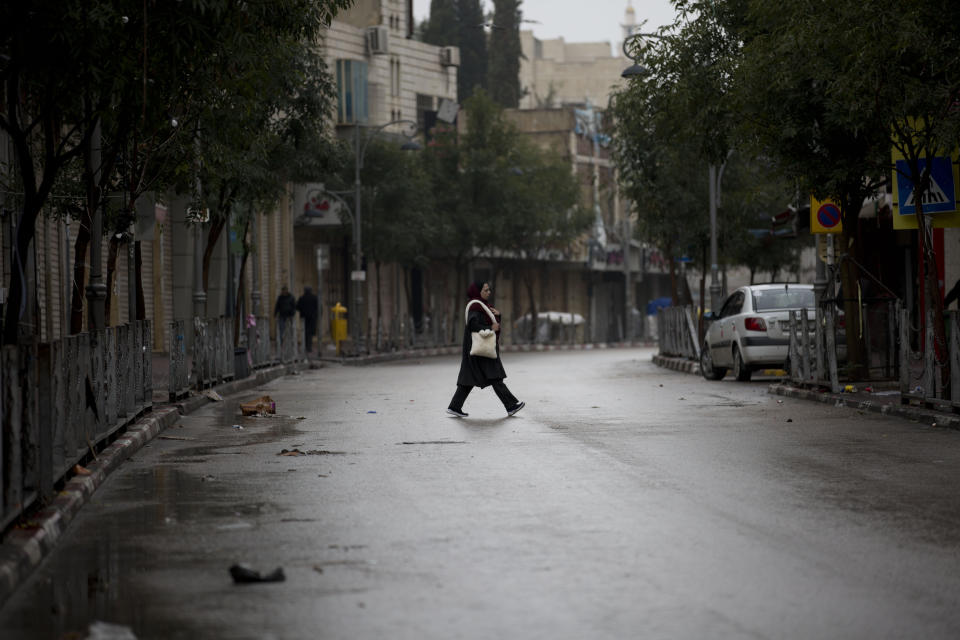 A Palestinian woman walks near closed shops during a general strike in the West Bank city of Hebron, Monday, Dec. 9, 2019. Palestinian residents held a general strike to protest an Israeli plan to build a new Jewish neighborhood in the heart of the West Bank's largest city. (AP Photo/Majdi Mohammed)