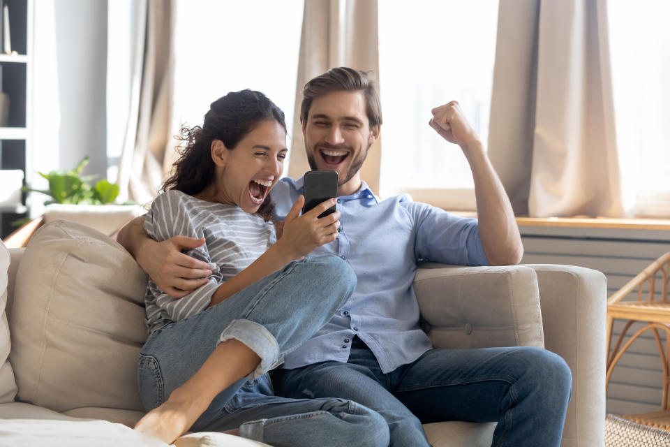 Woman and man sitting on couch, looking at mobile phone and celebrating