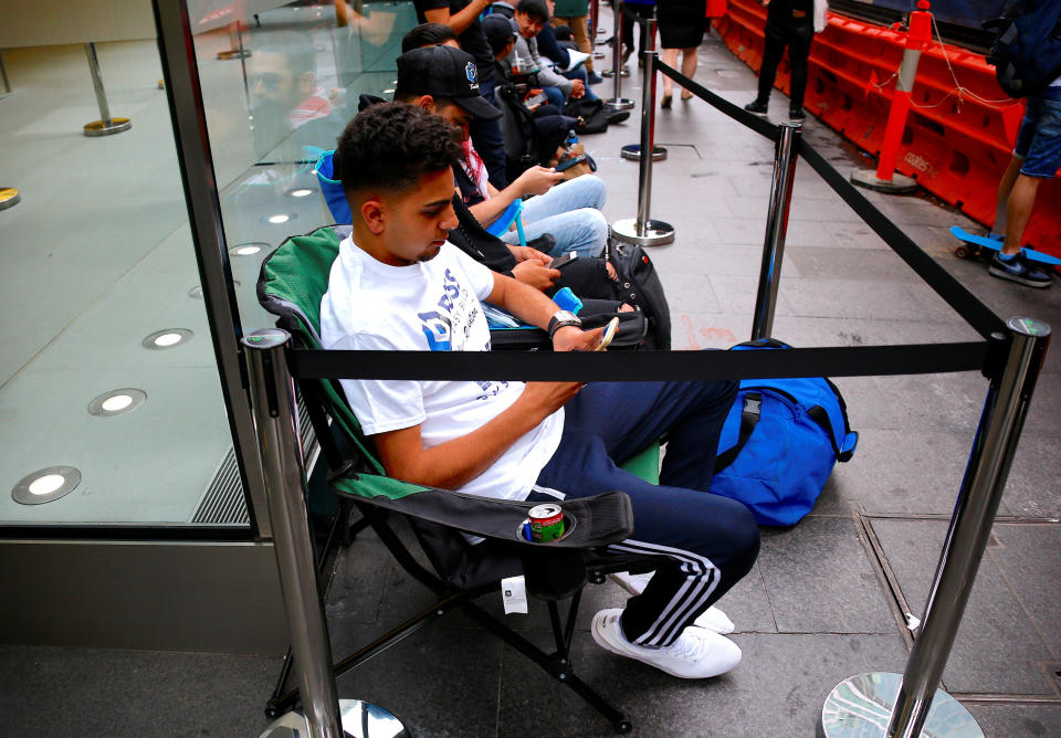 Customers sit in chairs using their iPhones as they wait in a line for the launch of the iPhone X during the global launch of the new Apple product in central Sydney