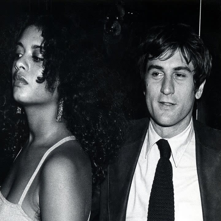 De Niro in the '70s looking pretty in a suit; a woman stands to his left