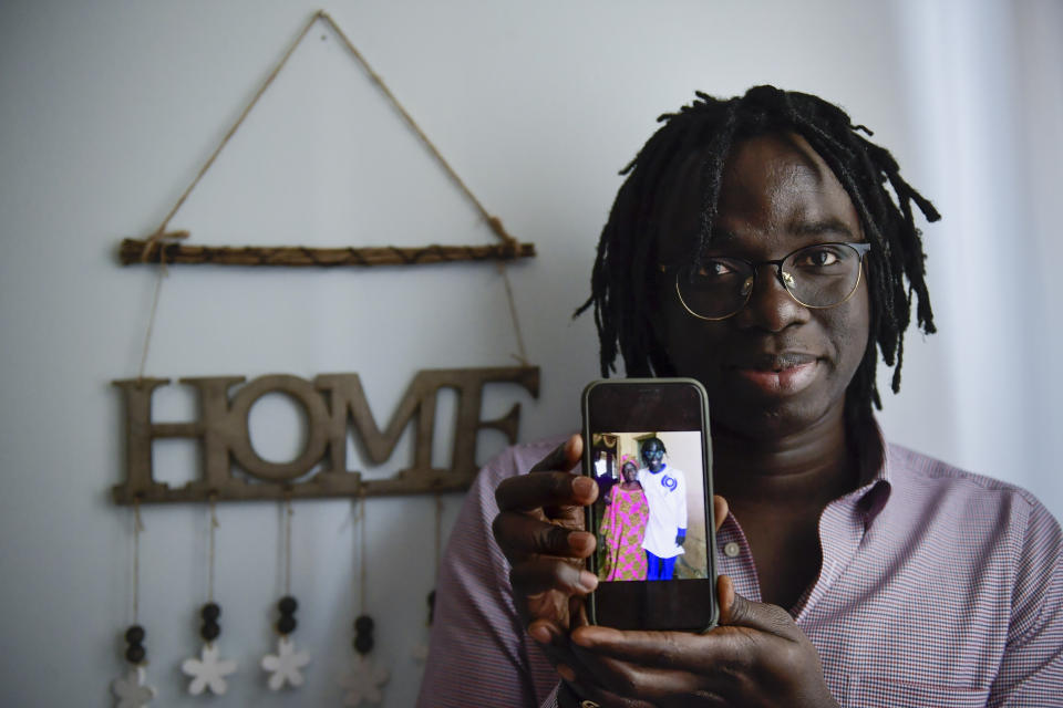 Mbaye Babacar Diouf, 33, displays a photo of himself with his Senegal's mother on a phone, in his house in the basque city of Algorta, northern Spain, Wednesday, Nov. 18, 2020. Mbaye Babacar Diouf's life as a migrant in Europe took a turn for the better when he was adopted in Spain at the age of 28. That enabled him to pay his debts to human traffickers, study nursing and find a job at a Spanish hospital. Now he's giving back to the community. In a Bilbao hospital he cares for COVID-19 patients. (AP Photo/Alvaro Barrientos)