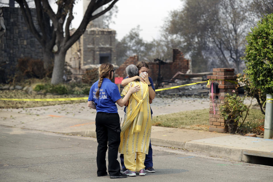 A resident, in yellow, wishing not to be identified, is comforted after seeing her fire-ravaged home for the first time Thursday, Aug. 2, 2018, in Redding, Calif. (AP Photo/Marcio Jose Sanchez)
