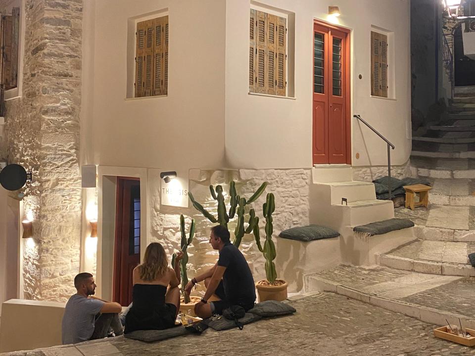 people sitting out on the steps outside theosis bar in syros greece