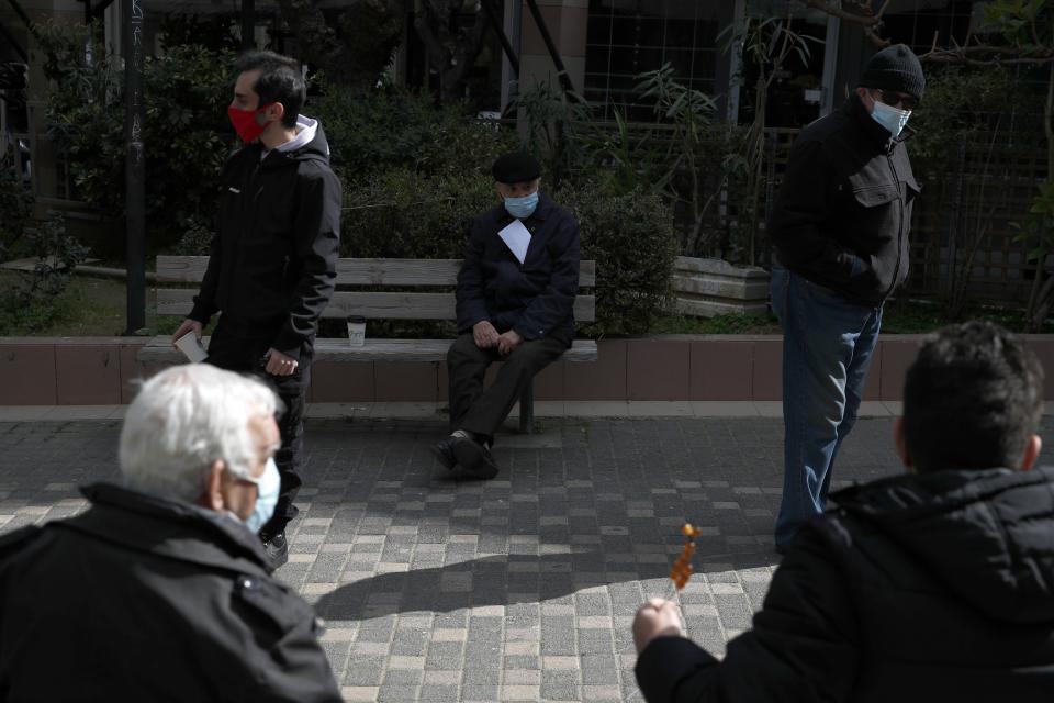 People sit on benches as others wait in a queue to conduct rapid tests for the COVID-19 in Athens, Wednesday, March 3, 2021. Greece has recorded a new spike in COVID-19 infections, nearly half of which were recorded in the greater Athens region where hospital intensive care units are quickly filling up. (AP Photo/Thanassis Stavrakis)