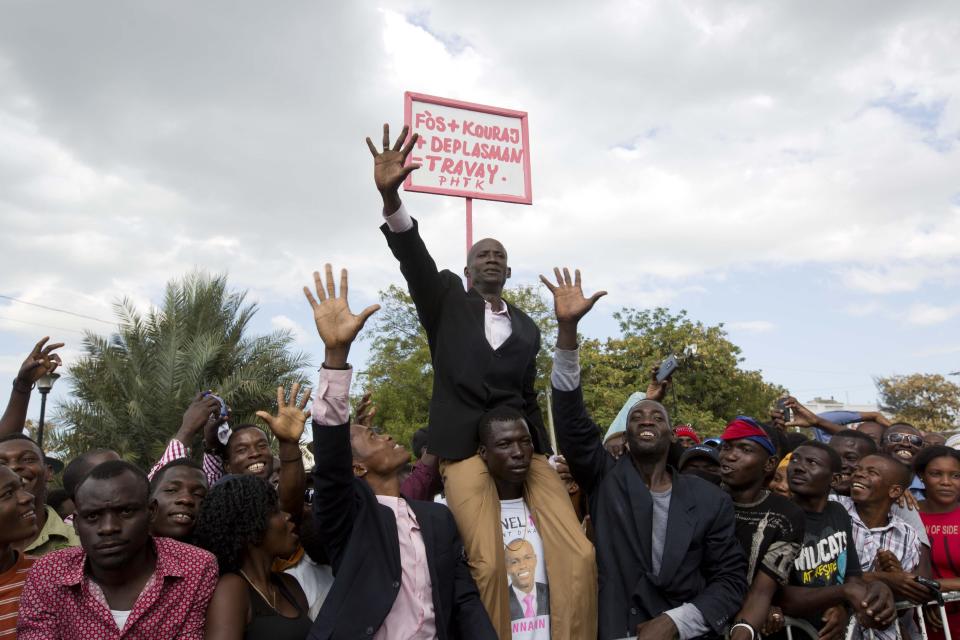 A supporter of Haiti's President Jovenel Moise impersonates the new president, with a sign behind him that reads in Creole "Energy plus encouragement plus movement plus work" during Moise's inauguration in Port-au-Prince, Haiti, Tuesday, Feb. 7, 2017. Moise was sworn-in as president for the next five years after a bruising two-year election cycle, inheriting a struggling economy and a deeply divided society. (AP Photo/Dieu Nalio Chery)