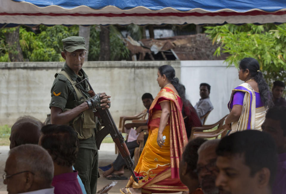 A soldier stands guard amid Catholics attending Mass outside St. Joseph's church in Thannamunai, Sri Lanka, Tuesday, April 30, 2019. This small village in eastern Sri Lanka has held likely the first Mass since Catholic leaders closed all their churches for fear of more attacks after the Easter suicide bombings that killed over 250 people. (AP Photo/Gemunu Amarasinghe)