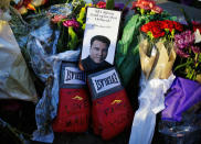 FILE - Boxing gloves and a message sit among flowers at a makeshift memorial to Muhammad Ali at the Muhammad Ali Center in Louisville, ky., in this Saturday, June 4, 2016, file photo. A new documentary looks at the city that raised Muhammad Ali, Louisville, Kentucky, and the week of his funeral, when the community came together to celebrate the legacy of “The Greatest.” (AP Photo/David Goldman, File)