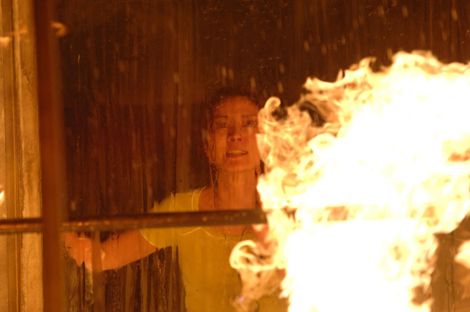 Michelle Yeoh stands near a wet window as a fire rises on the other side