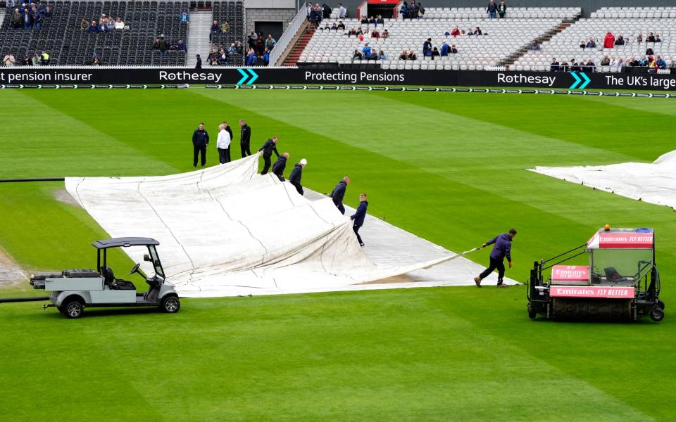 Umpires inspect the pitch as ground staff remove the rain covers during day two of the First Rothesay Test match at the Emirates Old Trafford