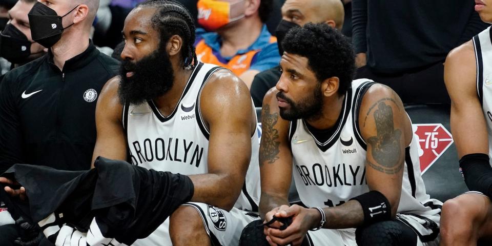 James Harden sits next to Kyrie Irving on the bench during a game in 2022.