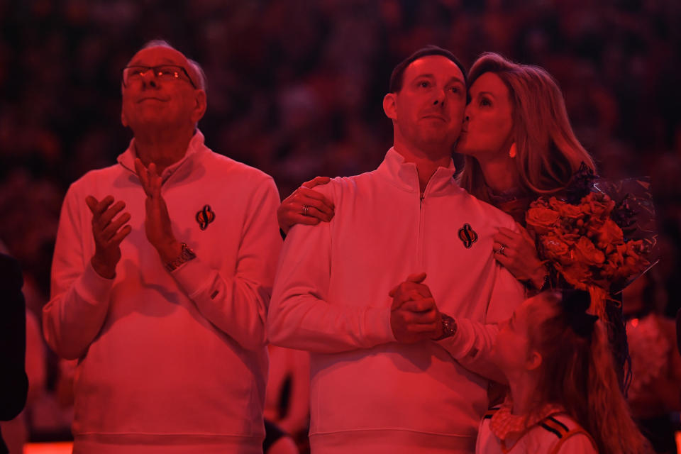 Syracuse assistant coach Gerry McNamara, center, gets a kiss from his wife Katie as he and head coach Jim Boeheim, left, watch McNamara's number be unveiled in the rafters of the JMA Wireless Dome after an NCAA college basketball game against Wake Forest in Syracuse, N.Y., Saturday, March 4, 2023. McNamara and 2003 national champion teammate Hakim Warrick had their numbers retired. (AP Photo/Adrian Kraus)