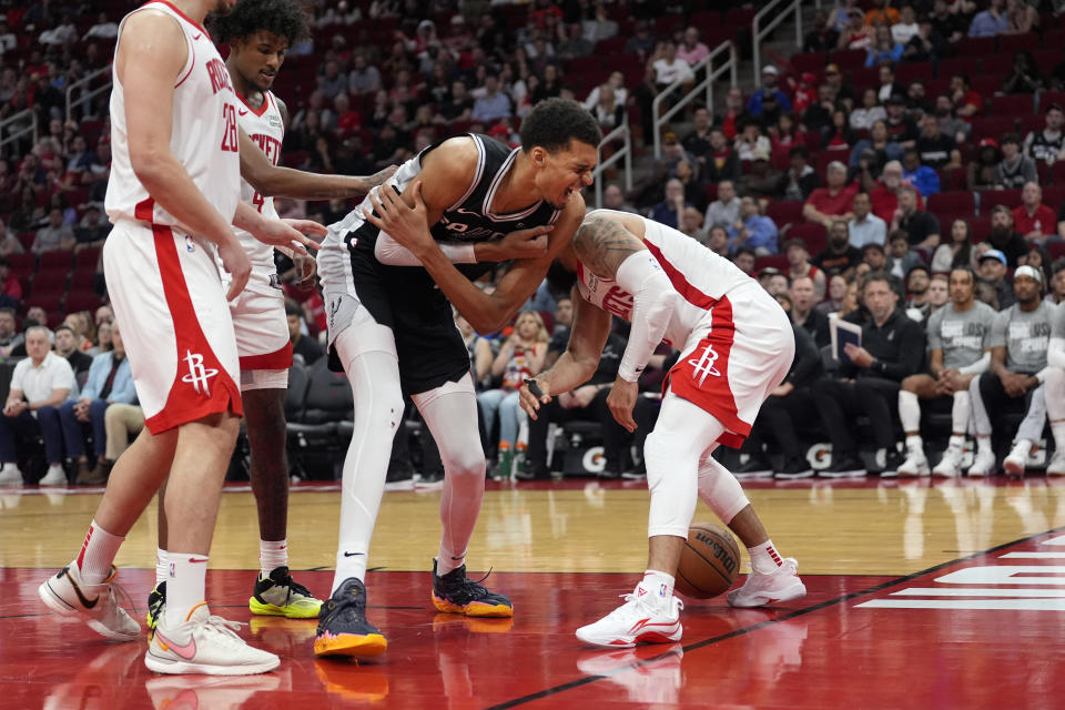 San Antonio Spurs' Victor Wembanyama, center, grabs his arm after losing the ball to Houston Rockets' Fred VanVleet, right, during the second half of an NBA basketball game Tuesday, March 5, 2024, in Houston. The Rockets won 114-101. (AP Photo/David J. Phillip)