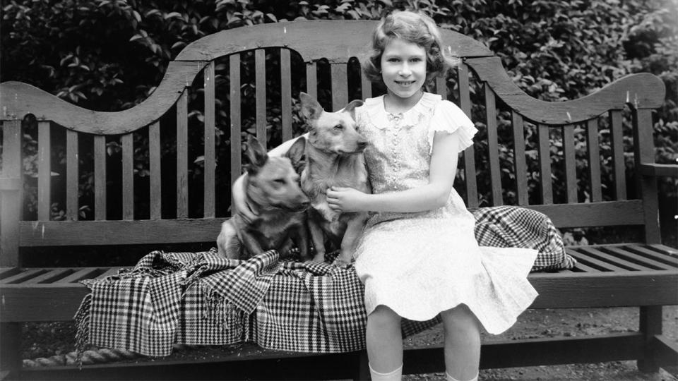 1936: Princess Elizabeth sitting on a garden seat with two corgi dogs at her home on 145 Piccadilly, London, in July 1936.