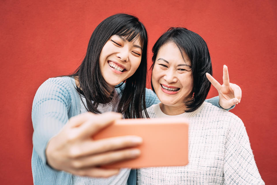 Happy Asian mother and daughter taking photo selfie with mobile smartphone outdoor.
