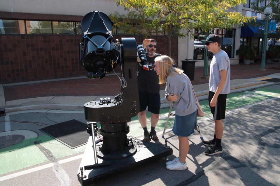 Morgan Andrews of Adrian looks through a telescope attached to a larger telescope Sept. 18, 2021, as Elijah Piekarela of Adrian looks on while Dan Medley, senior electrical engineer at PlaneWave Instruments, explains the telescopes at PlaneWave's exhibit at Artalicious in downtown Adrian.