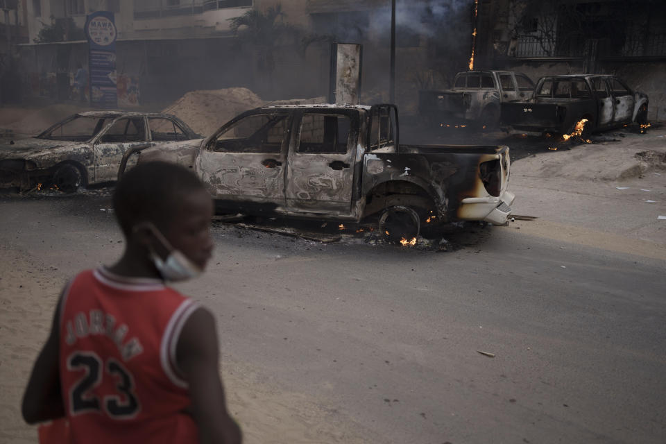 A young boy looks on as he stands next to burned cars during a protest in support of the main opposition leader Ousmane Sonko in Dakar, Senegal, Monday, May 29, 2023. The clashes came a day after police stopped Sonko's "freedom caravan," traveling from his hometown of Ziguinchor, in the south and where he is the mayor, to the capital, Dakar, where he was forced into a home he has in the city. (AP Photo/Leo Correa)