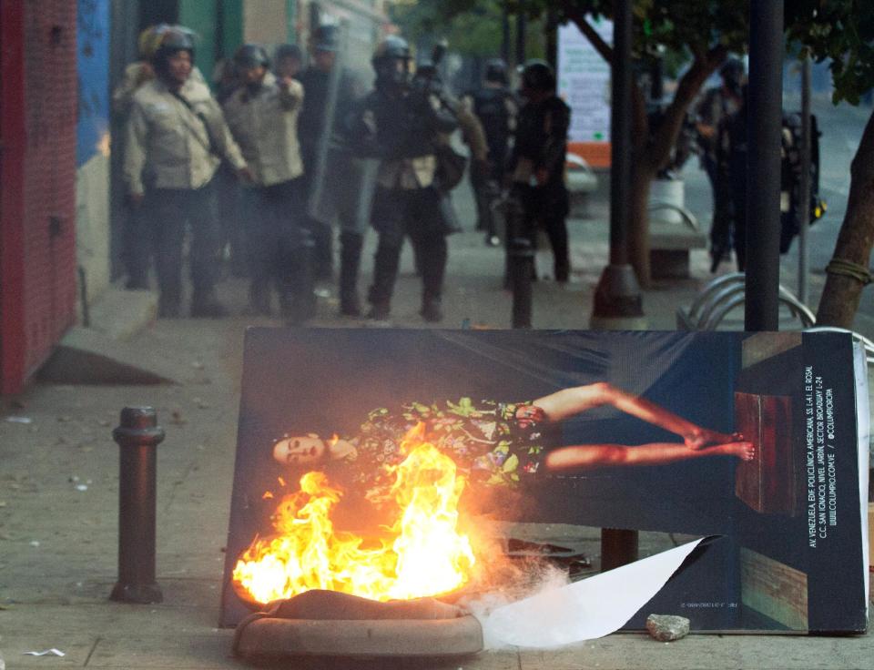 Bolivarian National policemen stand before a street advertisement set on fire by anti-government protesters during clashes in Caracas, Venezuela, Saturday, March 22, 2014. Two more people were reported dead in Venezuela as a result of anti-government protests even as supporters and opponents of President Nicolas Maduro took to the streets on Saturday in new shows of force. (AP Photo/Esteban Felix)