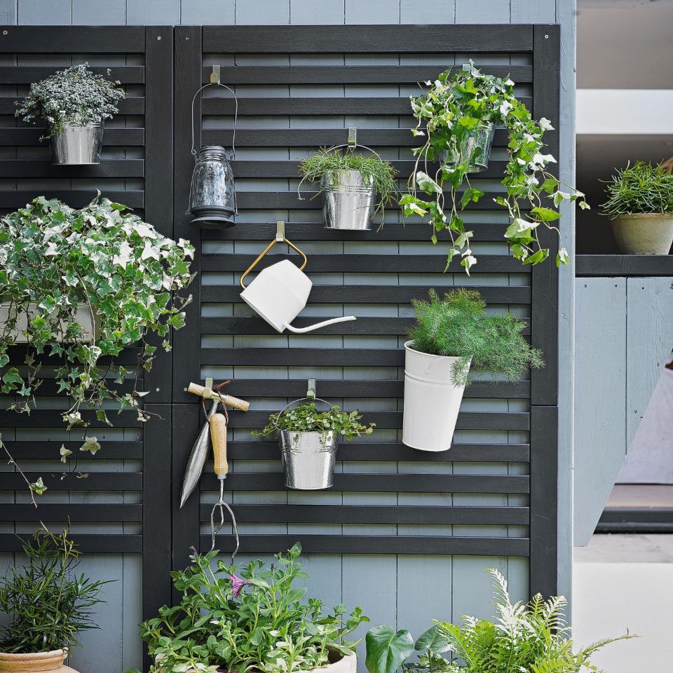 Garden tools and accessories hanging on black panelled garden wall