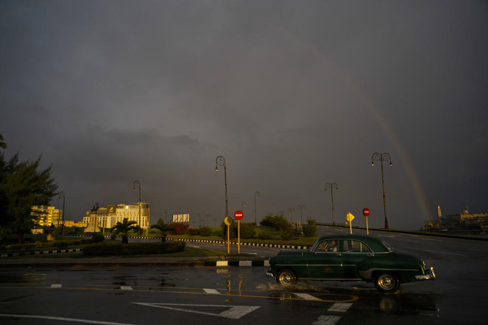 In this Nov. 10, 2019 photo, under a rainbow, a man drives a classic American car past the newly opened Hotel Paseo del Prado in Havana, Cuba. The city will celebrate its 500th anniversary on Nov. 16. (AP Photo/Ramon Espinosa)